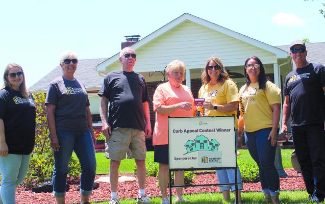 ELAINE PEDOCKIE (fourth from left) receives a gift card from the Hightower Heritage Real Estate team after being named the June 2025 winner of the Thrive Excelsior Curb Appeal Contest. The Pedockies were recognized for their self-maintained landscaping at 1014 Golf Hill Drive. MIRANDA JAMISON | Staff