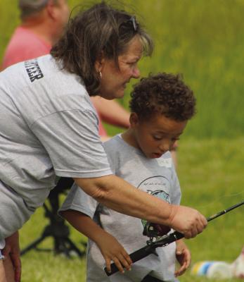 A VOLUNTEER SHOWS Taisto B. how to cast during a community fishing event. SHARON DONAT | Staff
