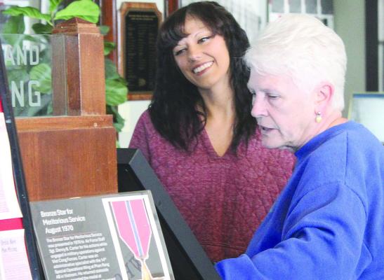 DEB FOSTER (right) explains the research and planning behind the “Not Forgotten” exhibit to lead reporter Miranda Jamison, discussing the process of matching newspaper archives with photographs and personal items from local families. SHARON DONAT | Staff
