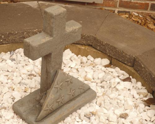 A cross with a folded flag sits in the center of the garden in remembrance of fallen veterans and their families.