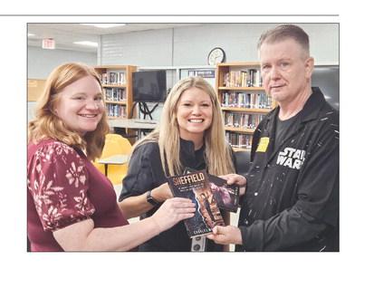 MIRANDA JAMISON | Staff EXCELSIOR SPRINGS WEST HIGH School graduate Charles Whitham (right) presents copies of his books to librarian Jessica Evert (left) and Principal Dr. Laura Hartman after speaking with students about his journey to becoming a published author.