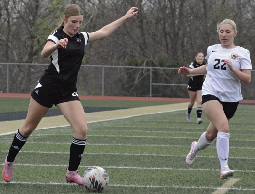 EMMALYN WHITE (left) looks to make a crossing pass for Excelsior Springs as Cameron sophomore Olivia Salgado closes in during tournament play at Tiger Stadium. SHAWN RONEY | Staff