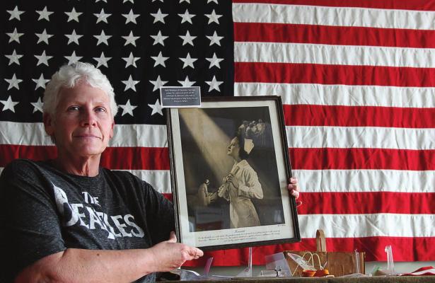 IN THE NEW World War II exhibition room, volunteer Deb Foster stands in front of a 48-star flag while holding a photograph of an Excelsior Springs woman, 2nd Lt. Nell Widmer, whose image assisted in the war effort.