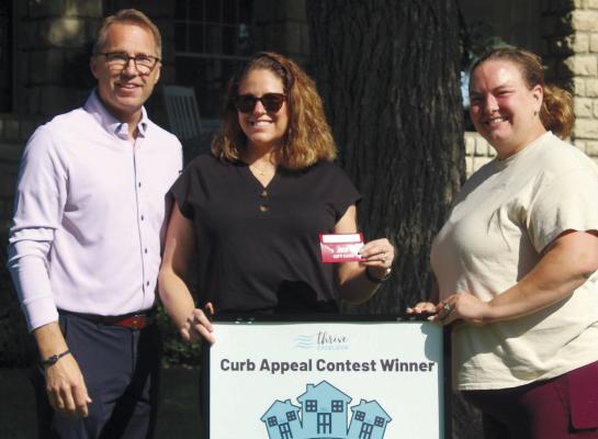 KEVIN (FROM LEFT) AND KRISTI RHINE of Ross Drive are recognized for their landscaping and property appearance as Thrive Excelsior Curb Appeal Contest winners. McClendon Seamless Guttering and Exteriors sponsored this month’s contest and co-owner Whitney Sparks presented the couple with a gift certificate. MIRANDA JAMISON | Staff