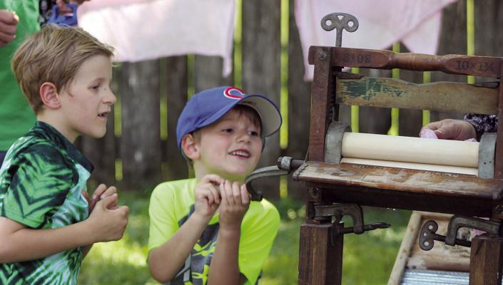 GRIFFON (LEFT) AND Kylan Sloop help feed laundry through a vintage wringer washer during Watkins Woolen Mill State Park’s annual Spring on the Farm event. SHARON DONAT | Staff