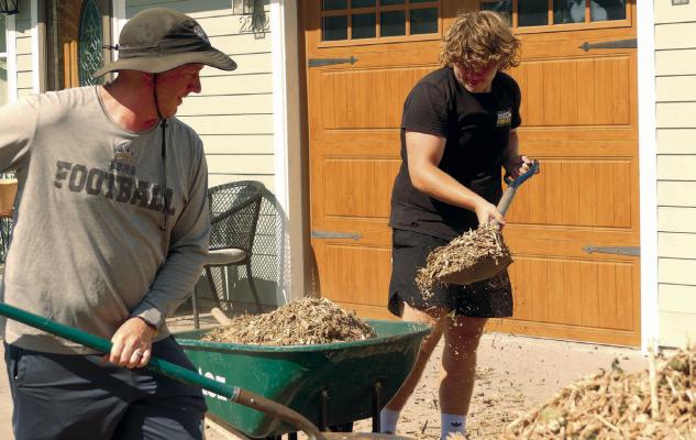 EXCELSIOR SPRINGS football coach Jonah Albertson and Brant Cashatt shovel mulch for Abigial Douglas’s vision of an English garden. ELIZABETH BARNT | Staff