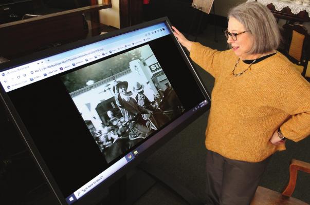 THIS NEW MONITOR at the Excelsior Springs Museum and Archives, shown by museum Director Kathy Duncan, provides video from a Mulesta Festival in the mid-1930s, including this cowboy with a six-shooter. J.C. VENTIMIGLIA | Staff