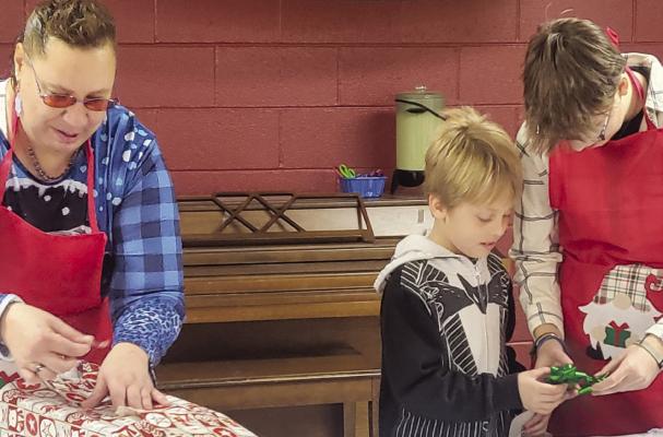 LAURIE BAKER (from left) wraps a gift while Jaxon Perry and Aniston Kennedy pick out the perfect bow.