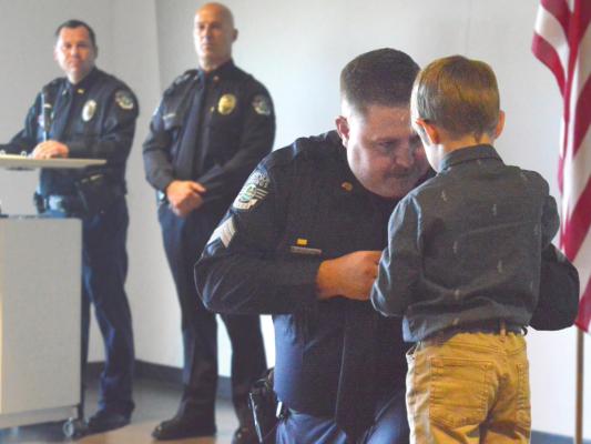KYLE CRAVEN kneels as his son Matthew pins a sergeant’s badge on him. Capt. Robert Warner and Chief Greg Dull, in the background, lead the July 27 promotion ceremony, advancing four officers from the rank of corporal to sergeant. TARA ALTIS | Staff