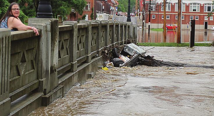 A COMMUNITY VISITOR, Melanie Cantwell, Springfield, stands on the Marietta Street Bridge while watching flash flood water from the Fishing River slap against the bridge bottom June 25, 2021. J.C. VENTIMIGLIA | Staff