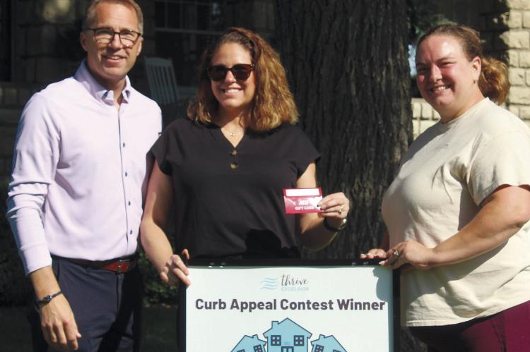 KEVIN (FROM LEFT) AND KRISTI RHINE of Ross Drive are recognized for their landscaping and property appearance as Thrive Excelsior Curb Appeal Contest winners. McClendon Seamless Guttering and Exteriors sponsored this month’s contest and co-owner Whitney Sparks presented the couple with a gift certificate. MIRANDA JAMISON | Staff
