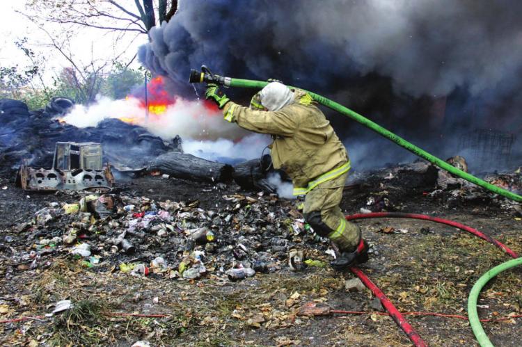 AFTER ATTACKING the front of a burning structure, a volunteer firefighter drags a hose to reach another hot spot. Among several fire departments that respond to the blaze on Highway O in October 2018 is Wood Heights, which seeks passage of Prop A to maintain the volunteer department’s ability to fight fires with critical safety equipment, Chief Lee O’Dell says. J.C. VENTIMIGLIA | Staff