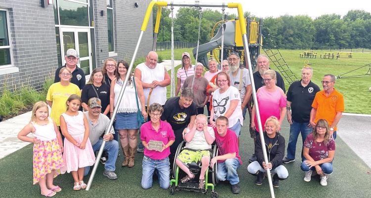 DIANA REINERT (kneeling, pink shirt), Cheryl Mick (behind Reinert) and members of the Excelsior Springs Fraternal Order of Eagles donate a wheelchairaccessible, adaptive swing to Cornerstone Elementary. Trying out the swing is Bently Ford, 10, with father Travis Ford and mother Sarah Loveall beside him. BRIAN RICE | Staff
