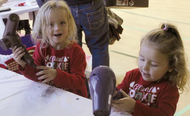 LILLY (LEFT) AND Emmy Remboldt blow-dry their handprint creations at the Elf Factory event hosted at the Community Center. MIRANDA JAMISON | Staff