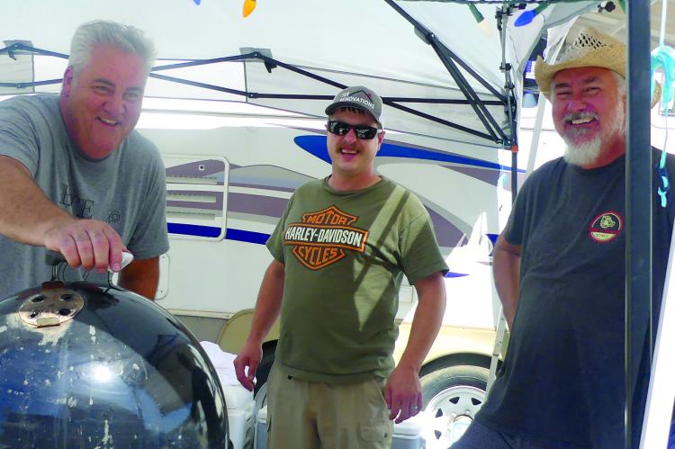 ROB MULLER (from left), Tyler Kerns and Ron Muller shut the lid to their smoker while cooking.