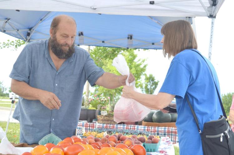 DWAYNE GRASS hands over a bag of fresh produce to Becky Cowsert on a Wednesday morning at the Excelsior Springs Community Center’s Farmers Market. TARA ALTIS | Staff