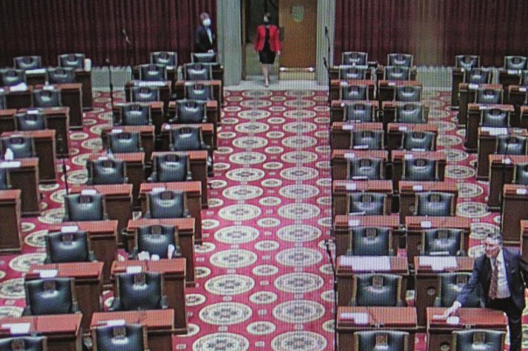THE HOUSE CHAMBER, ordinarily packed like a university lecture hall, with members sitting side-by-side at their desks, is eerily quiet, being almost empty as individual representatives enter, go to their desks, punch a button to cast a vote and leave. Like almost all of the representatives, Rep. Peggy McGaugh casts her vote while wearing a safety mask.