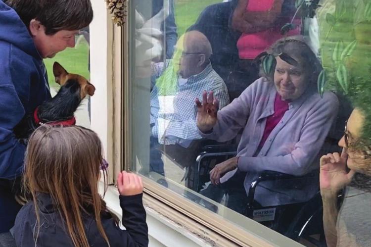AT A WINDOW at the Valley Manor Nursing &amp; Rehabilitation Center, visitors and their dog offer comfort to facility residents during the Valley Manor pet parade.
