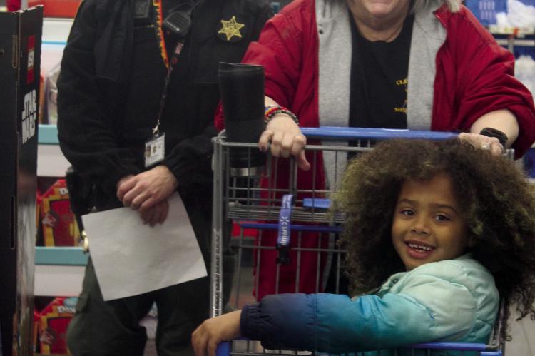 DEPUTY RYAN MCPHEETERS (from left) and records clerk Tracey Happy brings a child participant toward the toy aisles.
