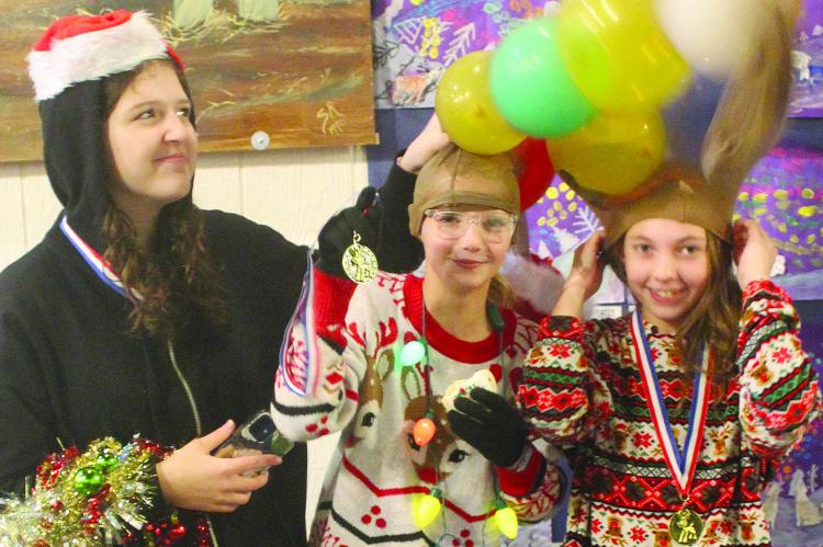 AUDREY THOMAS (from left), Myer McNary and Isabella Schoeneck try to keep their antlers standing up straight after participating in a contest at Orrick’s Old Fashion Christmas.