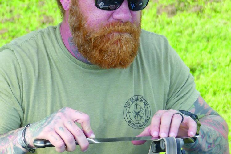 PHILIP KILPATRICK sharpens knives at his booth, Tip of the Spear, for farmers market patrons.