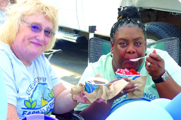 FARMERS MARKET director Tammy Murphey and Janet Wesley, farmers market coalition member, enjoy shaved ice for National Farmers Market Week.