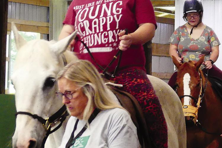 VOLUNTEER LYNN MAYABB (front) leads Kylee Rotert and her sister, Abigail, as they take a riding lesson at Northland Therapeutic Riding Center.