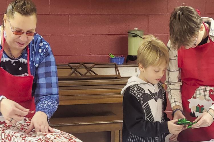 LAURIE BAKER (from left) wraps a gift while Jaxon Perry and Aniston Kennedy pick out the perfect bow.