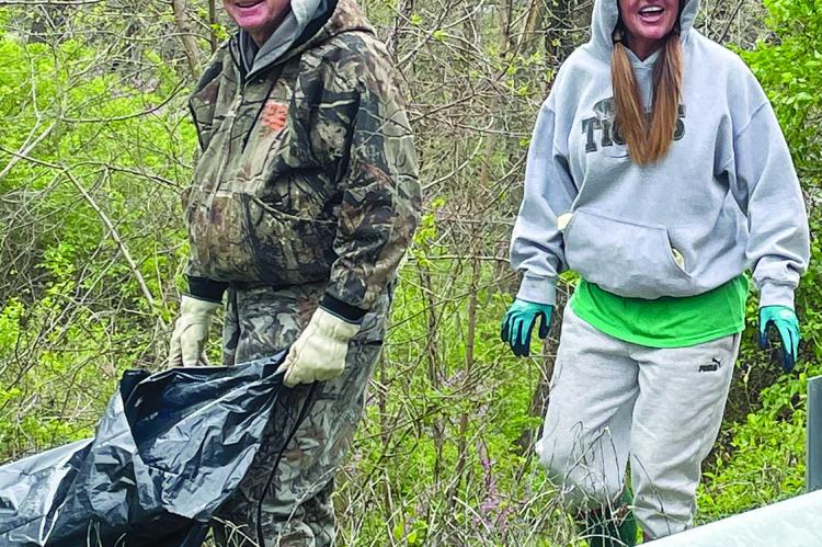 MIKE EDWARDS HAULS a trash bag as Kim McElwee-Sanson helps collect trash.